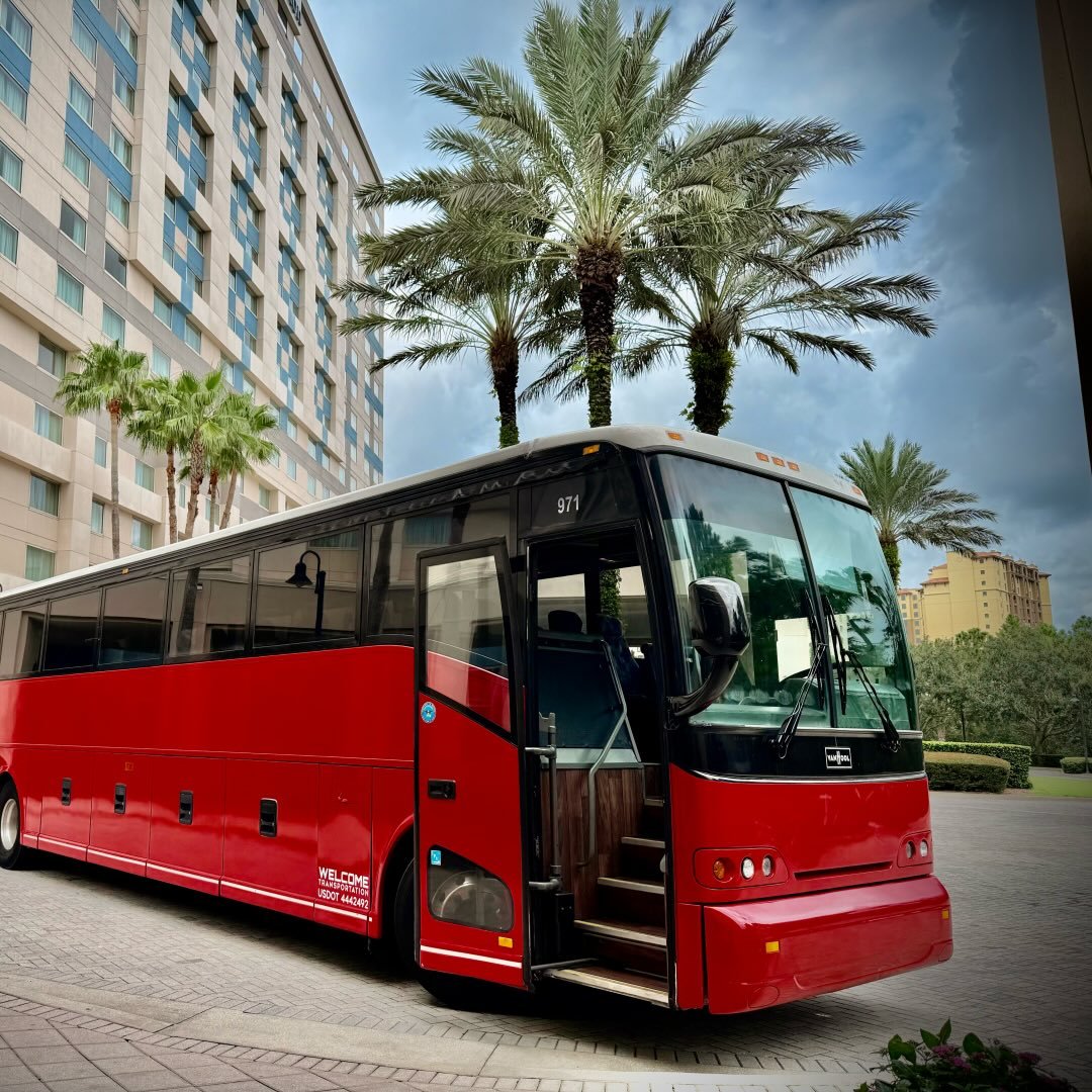 Welcome Transportation bus parked among palm trees at a resort entrance