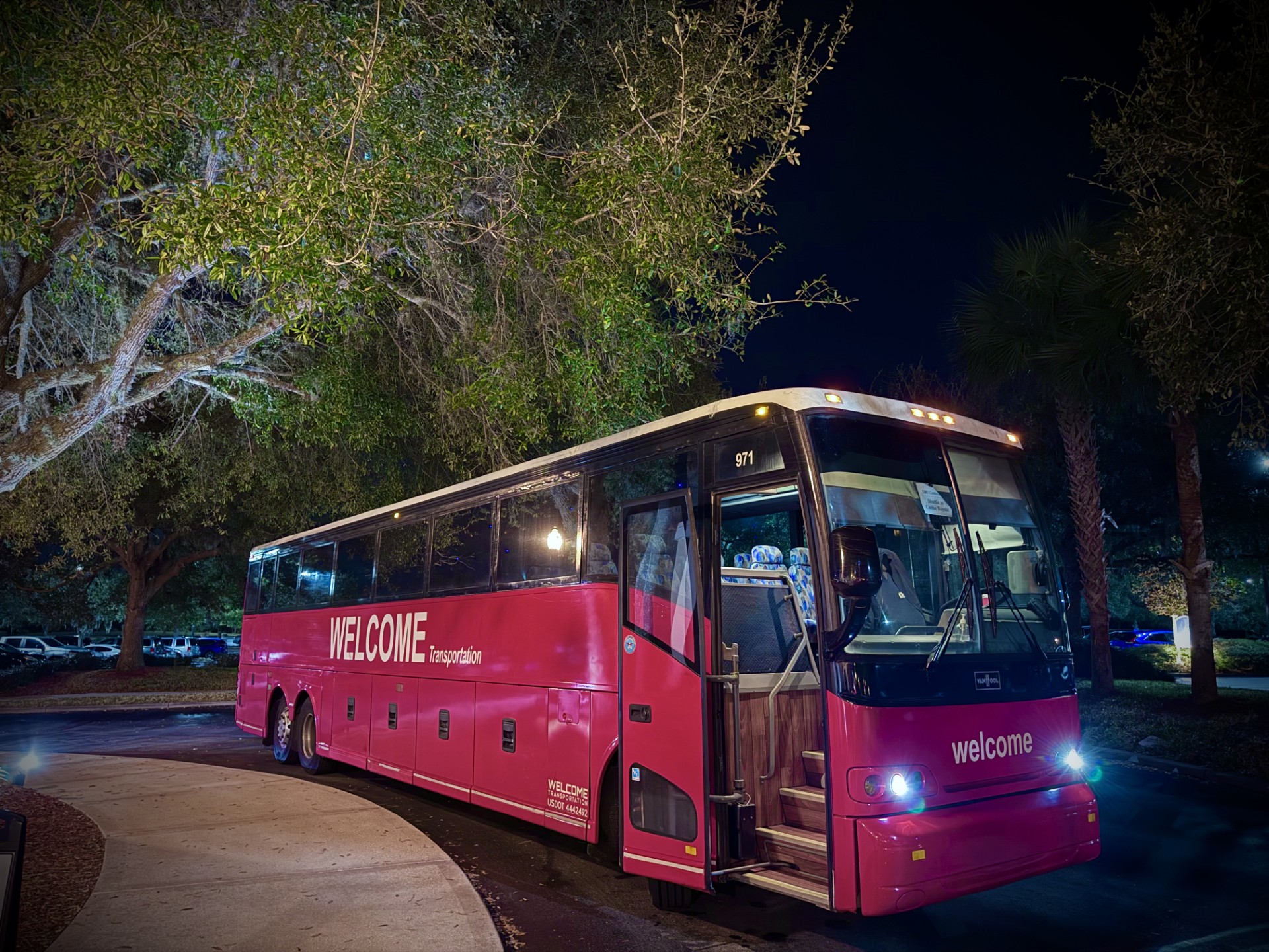 Welcome Transportation bus parked under oak trees at a resort at night