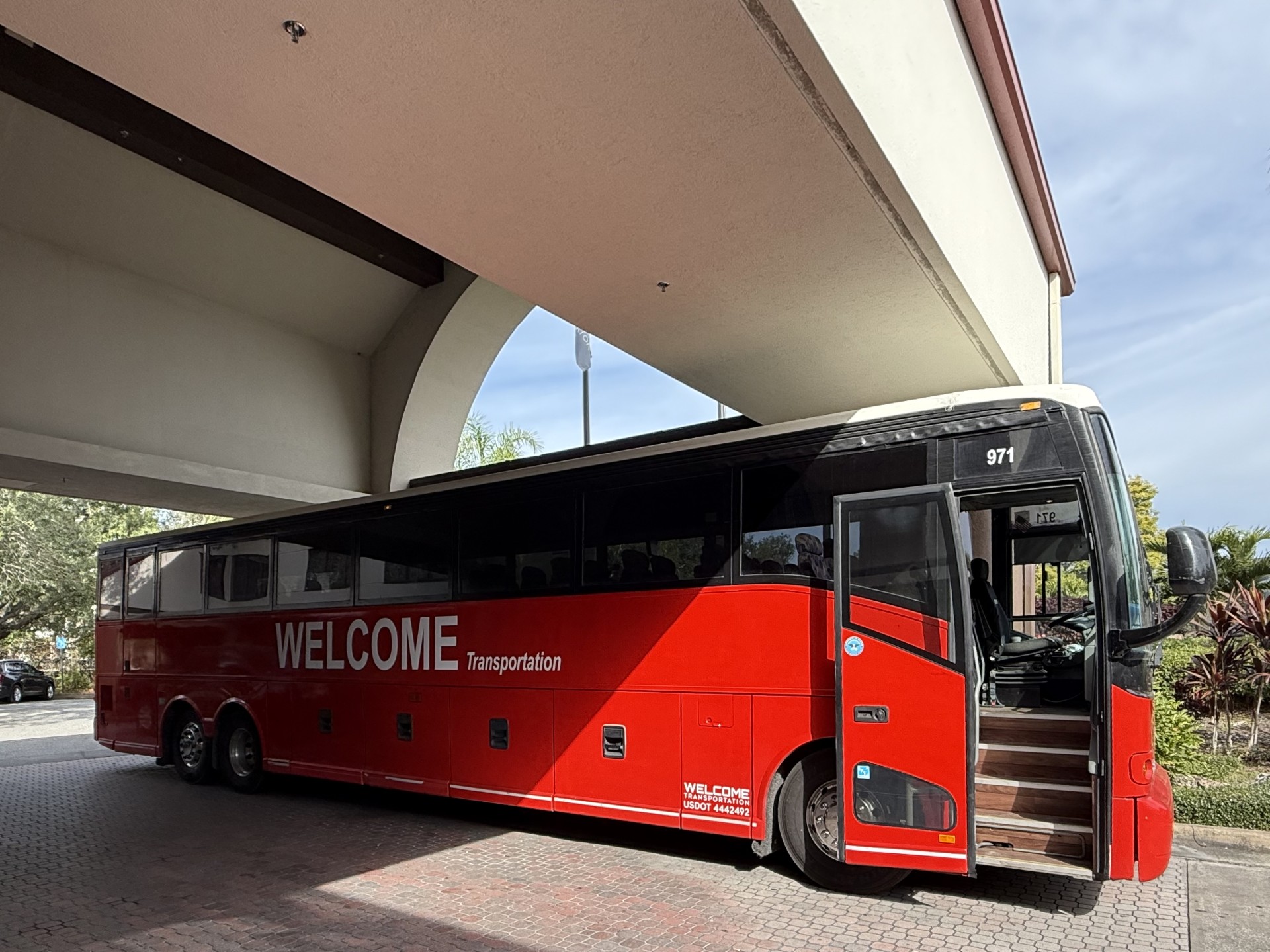 Welcome Transportation bus parked under a hotel entrance canopy in daylight