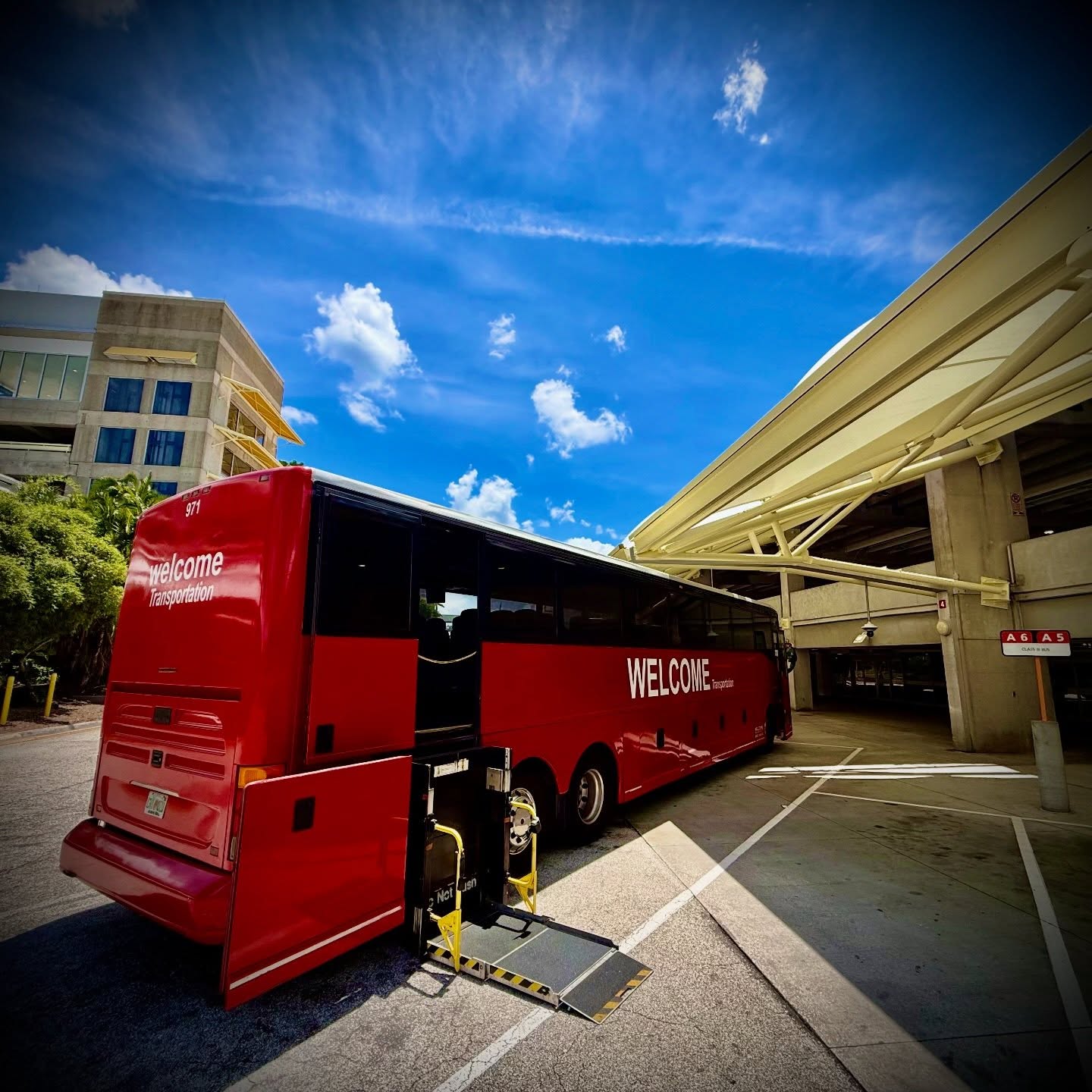Welcome Transportation bus with wheelchair lift extended under a parking garage canopy