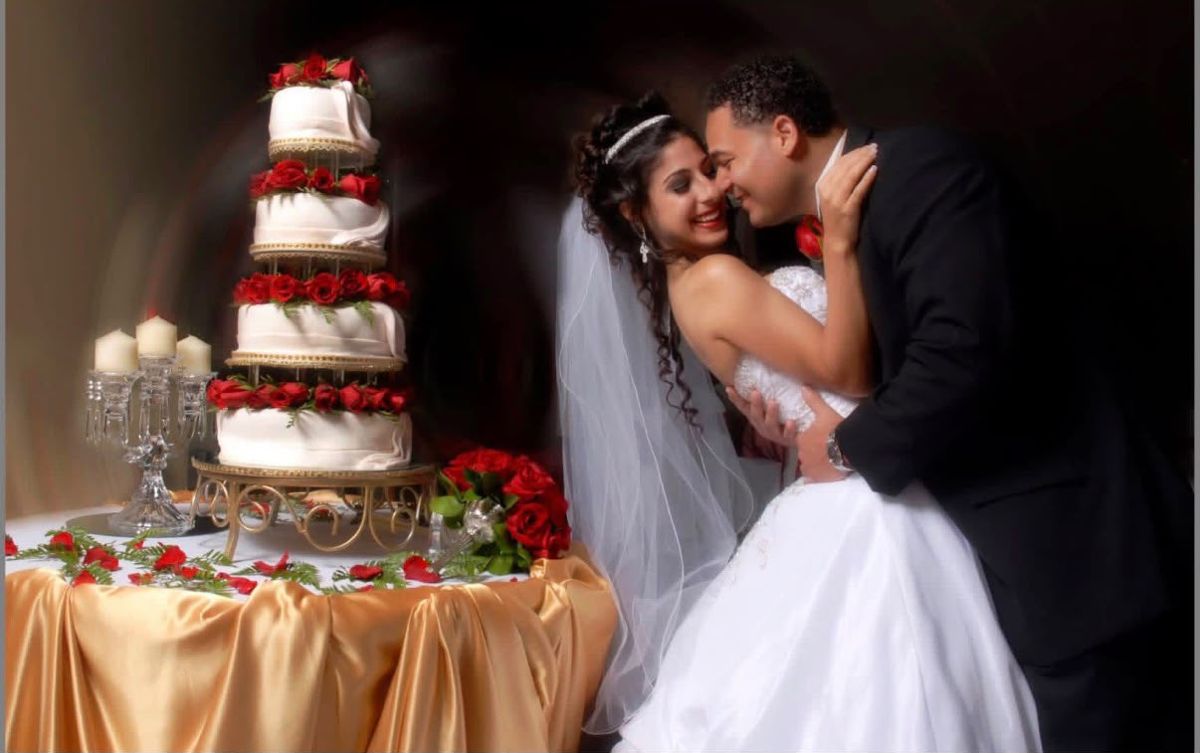 Bride and groom beside a tiered wedding cake with red roses